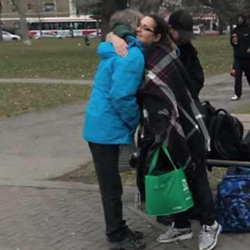 Two women hugging on a sidewalk near a park.