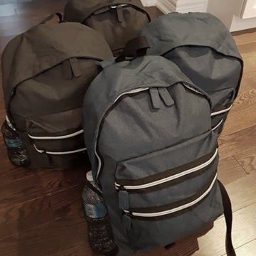 Three backpacks are sitting on the floor next to a bottle.